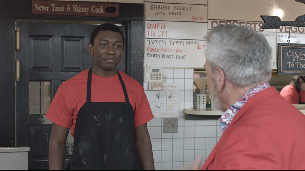 Two men talking in a diner. The man on the left is wearing a black apron.